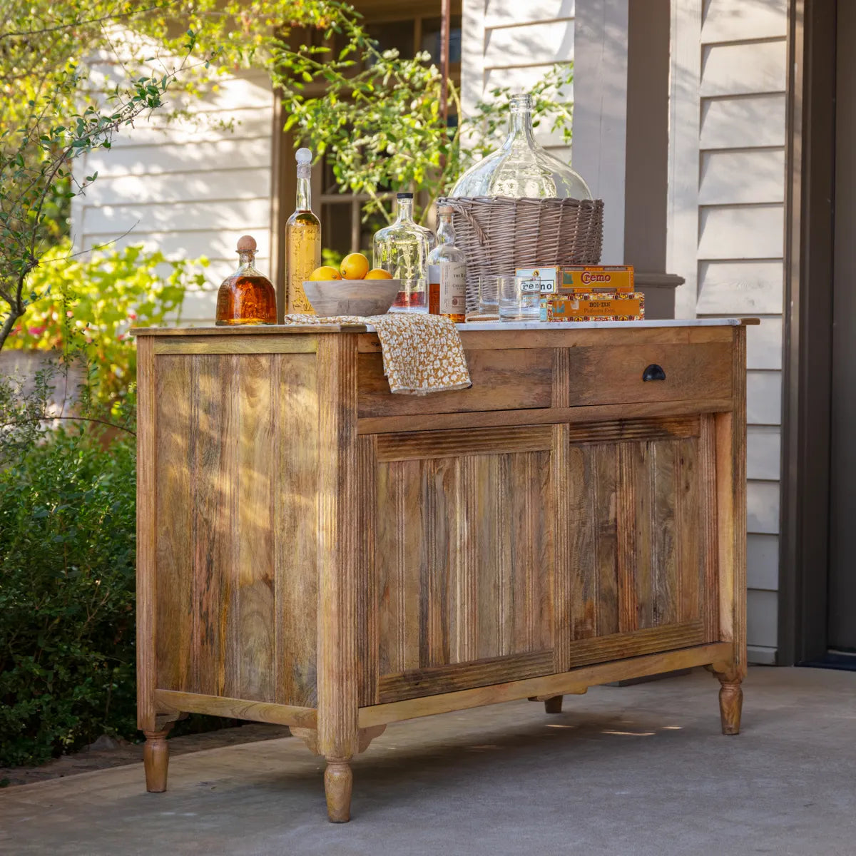 A brown wooden patisserie work counter with a white marble top, displayed outdoors with decorative items on top.